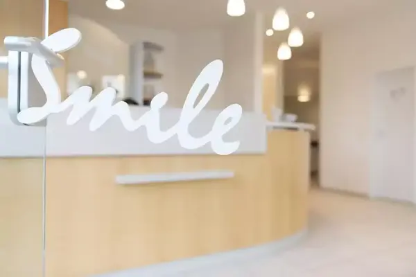 Heller Empfangsbereich einer Zahnarztpraxis mit dem Schriftzug "Smile" auf Glastür.