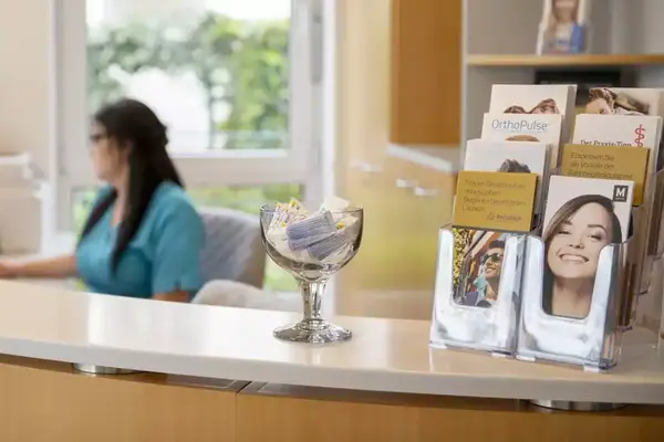Heller Empfangsbereich einer Zahnarztpraxis mit Broschüren und einer Mitarbeiterin am Tresen.