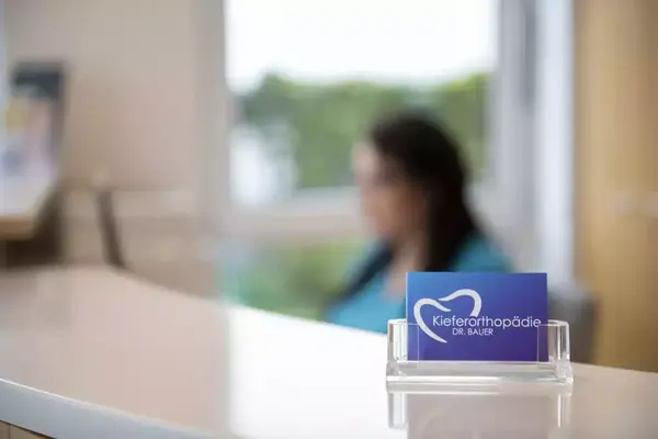 Visitenkarte einer Kieferorthopädie Praxis auf einem Tresen mit unscharfer Frau im Hintergrund.
